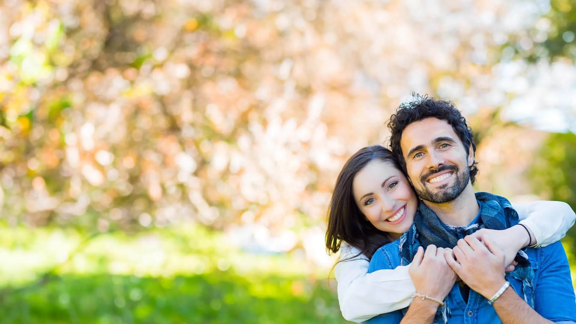 Happy young couple embracing outdoors with blurred spring foliage background and warm sunlight
