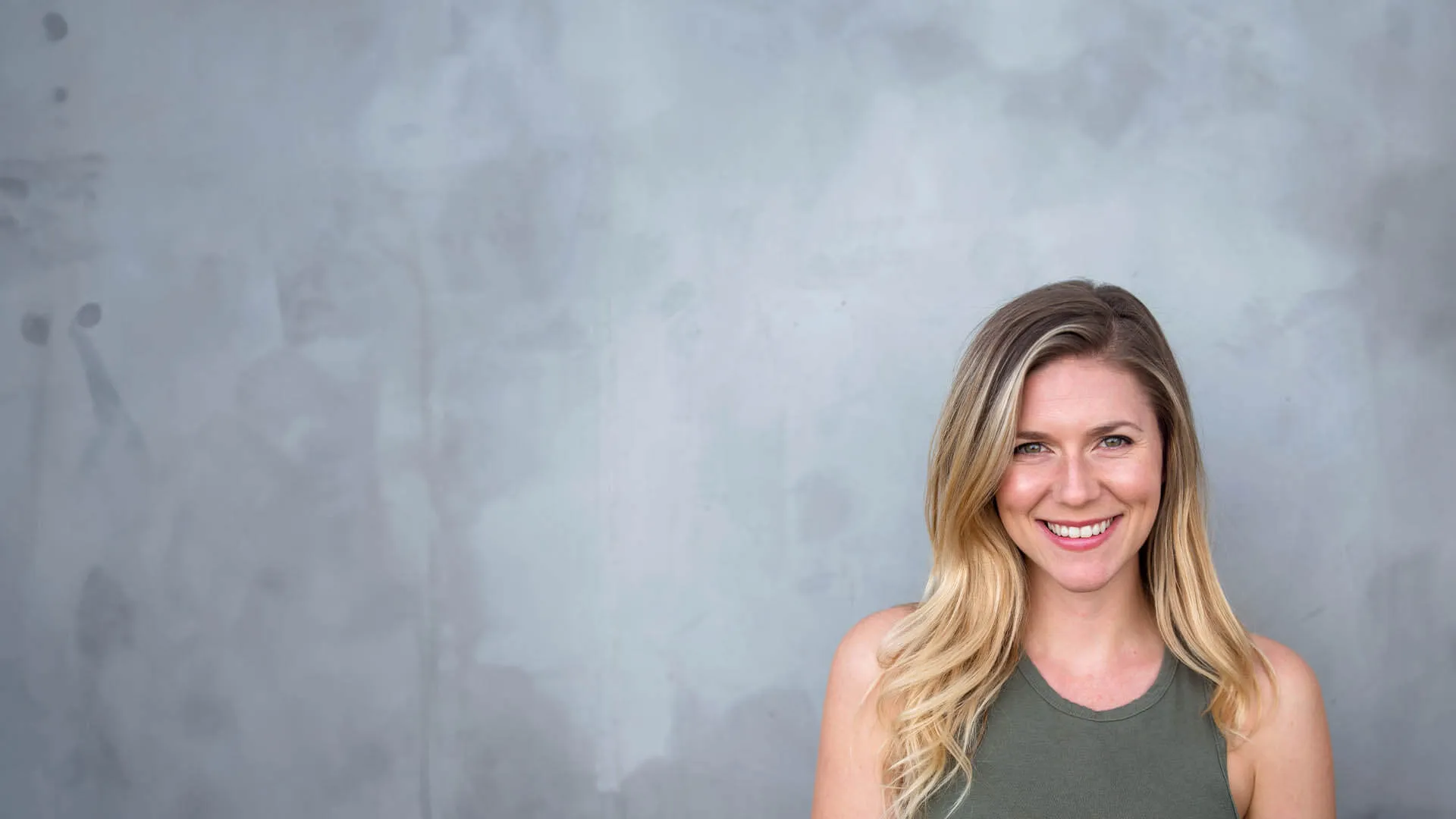 a woman smiling in front of a grey wall
