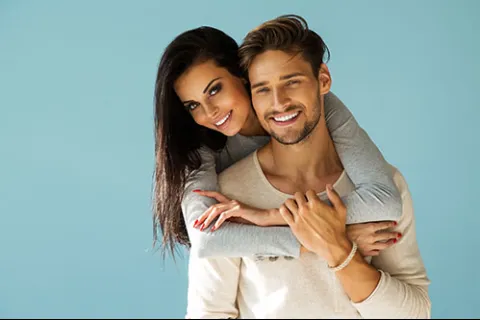 Happy young couple smiling and embracing against a blue background, showing affection and closeness
