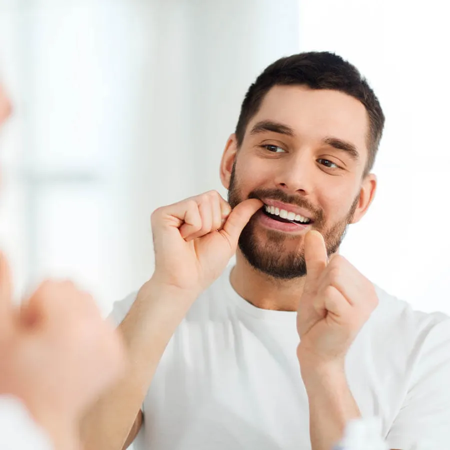 Man with beard flossing his teeth in front of a mirror for oral hygiene.