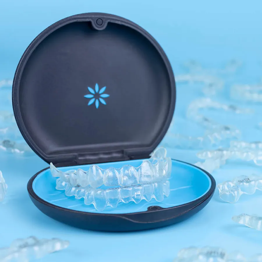 Clear dental aligners displayed in an open black and blue carrying case on a light blue background.