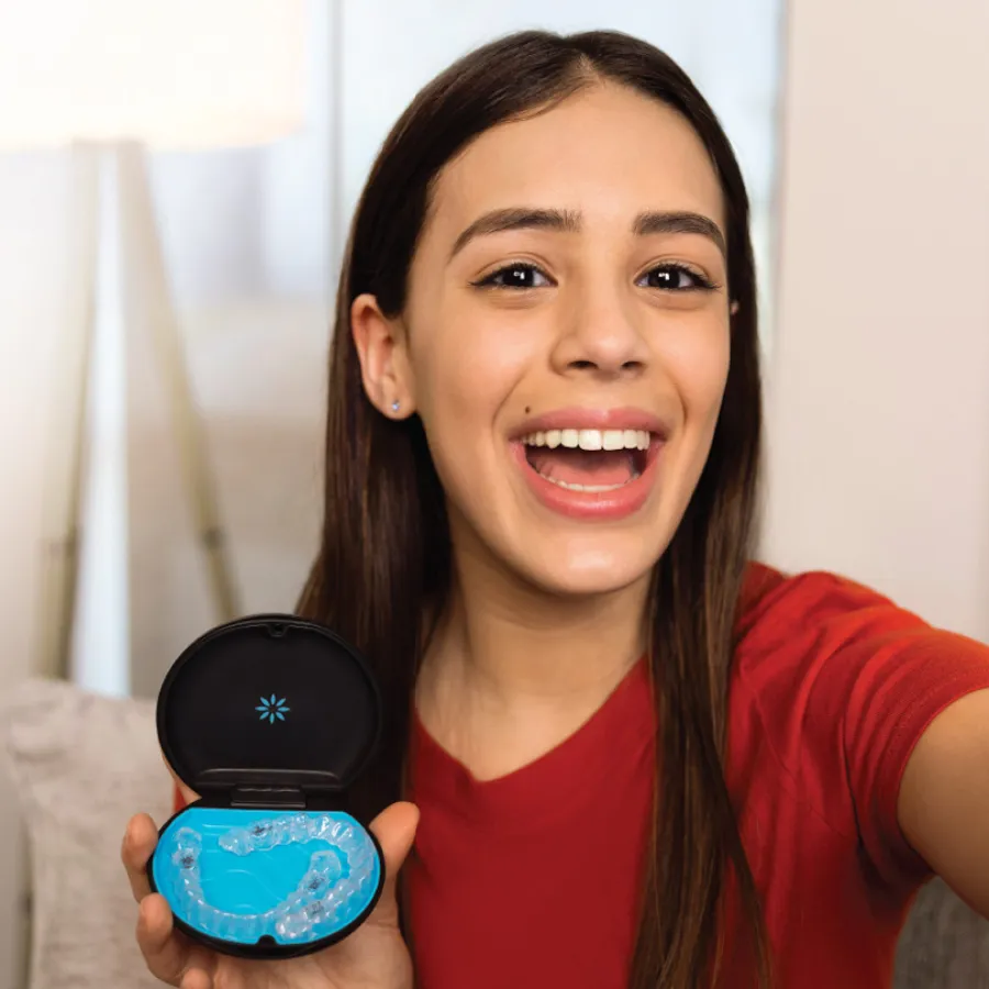 Smiling young woman holding clear dental aligners in a black case with a blue interior, wearing a red shirt.