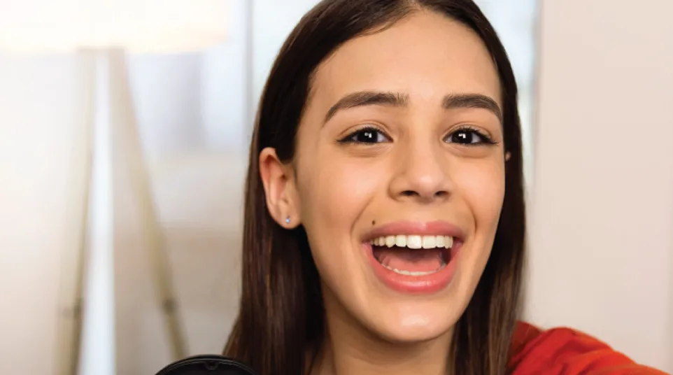 Smiling young woman holding clear dental aligners in a black case with a blue interior, wearing a red shirt.